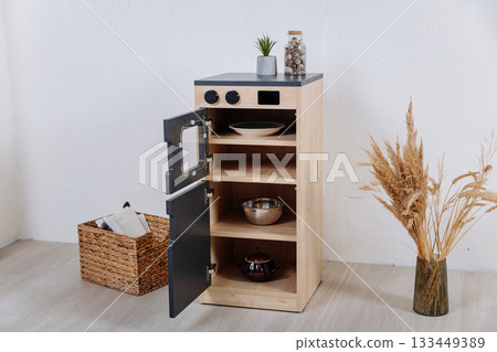 Wooden toy kitchen cabinet with open doors and shelves in minimalist kids room Wooden toy kitchen cabinet with open doors and shelves in minimalist kids room 133449389