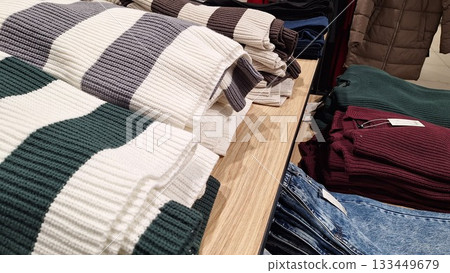 Folded striped and solid knit sweaters displayed on a wooden table in a cozy clothing store 133449679