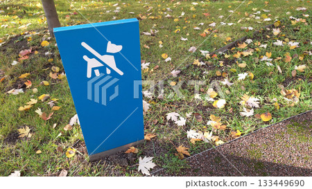 Blue outdoor sign with a crossed-out dog symbol indicating no pets allowed on grass 133449690