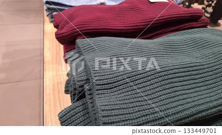 Neatly folded ribbed knit sweaters in deep red and olive green displayed on a retail shelf 133449701
