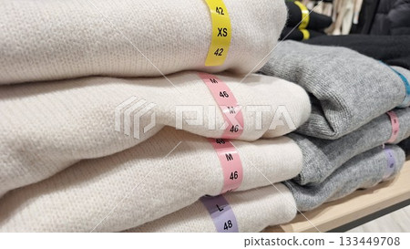 Neatly folded stack of sweaters labeled with various sizes for retail clothing display Neatly folded stack of sweaters labeled with various sizes for retail clothing display 133449708
