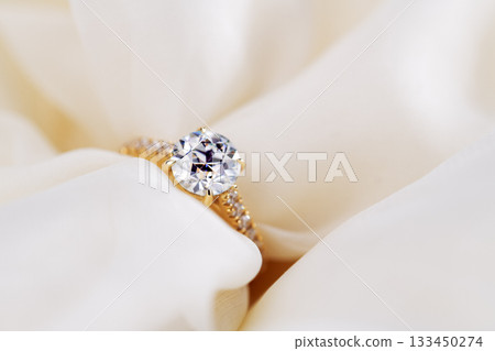 A gold and white diamond ring is on a white cloth 133450274