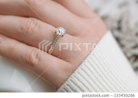 A woman is wearing a gold and diamond ring on her finger A woman is wearing a gold and diamond ring on her finger 133450286
