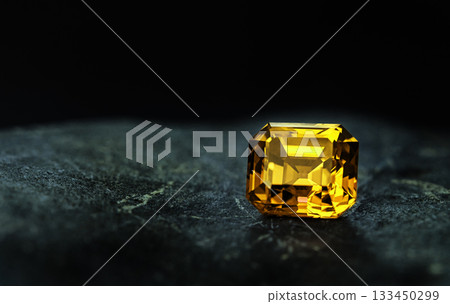 A yellow gemstone sits on a dark surface A yellow gemstone sits on a dark surface 133450299