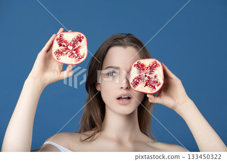 Beautiful young woman covering her eye with pomegranate fruit slices 133450322