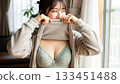 A woman in green underwear flips her clothes and laughs happily by the window 133451488