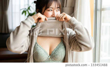A woman in green underwear flips her clothes and laughs happily by the window 133451488