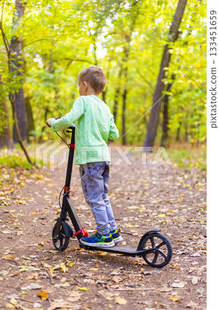 Child Riding Scooter on Forest Path in Autumn Child Riding Scooter on Forest Path in Autumn 133451659