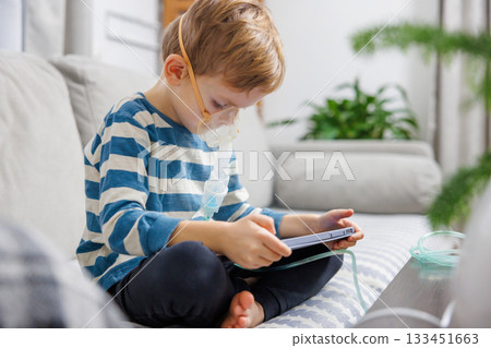 Child Using Nebulizer While Playing on Tablet at Home Child Using Nebulizer While Playing on Tablet at Home 133451663