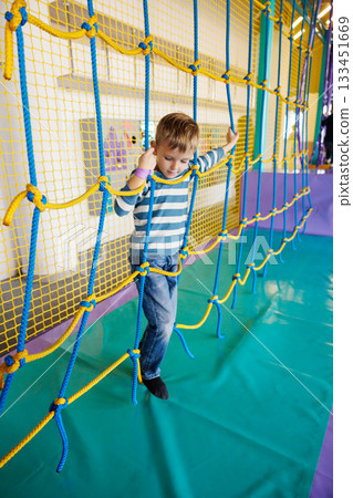 Child Enjoying Rope Climbing Adventure in Indoor Playground Child Enjoying Rope Climbing Adventure in Indoor Playground 133451669