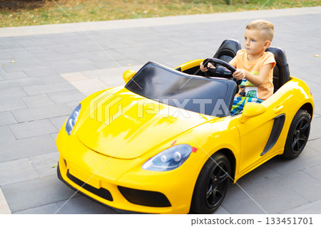 Child Enjoying Ride in Yellow Toy Car on Pavement Child Enjoying Ride in Yellow Toy Car on Pavement 133451701