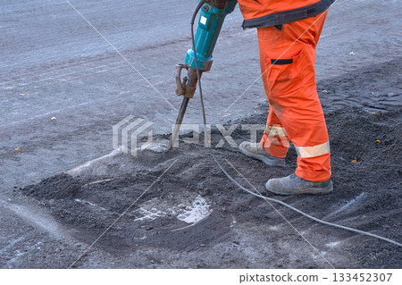 Repair.A road worker breaks up old asphalt with a jackhammer 133452307
