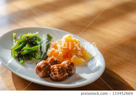 A breakfast plate with meatballs, mentaiko potatoes, and a side dish of bell peppers 133452669