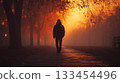 A lone person walks down a foggy path surrounded by trees at sunset. Concept of solitude and contemplation. For expressing introspective moods 133454496
