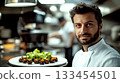 Chef in a kitchen holding a plate of gourmet food. Concept of culinary expertise and fine dining. For culinary articles or restaurant promotions. 133454501