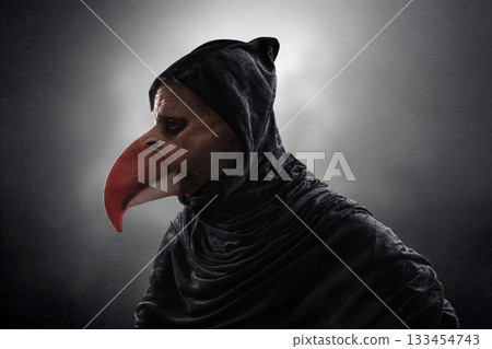 Creepy figure with long bird beak in hooded cloak over dark misty background Creepy figure with long bird beak in hooded cloak over dark misty background 133454743