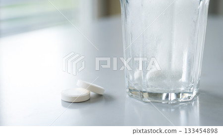 Soluble tablets. Glass of water with dissolving pills on white table 133454898