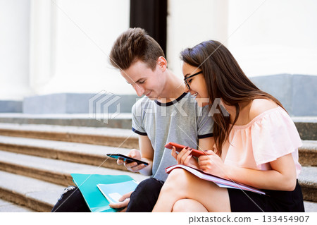 Student friends watching something funny on a smartphone - Best friends laughing and having fun outdoors Student friends watching something funny on a smartphone - Best friends laughing and having fun outdoors 133454907