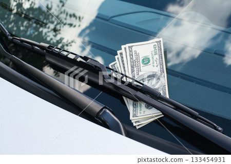 Bundle of US dollar banknotes left on a car under the car wiper on a windscreen Bundle of US dollar banknotes left on a car under the car wiper on a windscreen 133454931