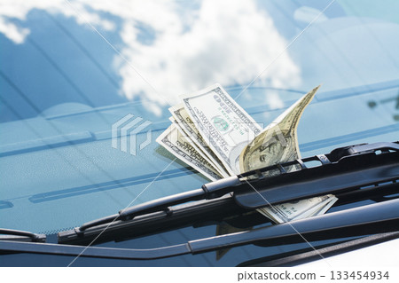 Bundle of US dollar banknotes left on a car under the car wiper on a windscreen Bundle of US dollar banknotes left on a car under the car wiper on a windscreen 133454934