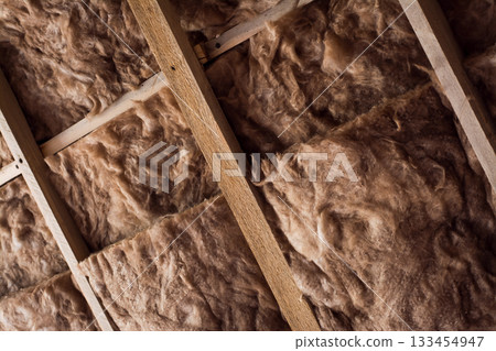 Fiberglass is used as warming material on a ceiling in a private house. Glass wool in a wooden frame on a wall. Fiberglass is used as warming material on a ceiling in a private house. Glass wool in a wooden frame on a wall. 133454947
