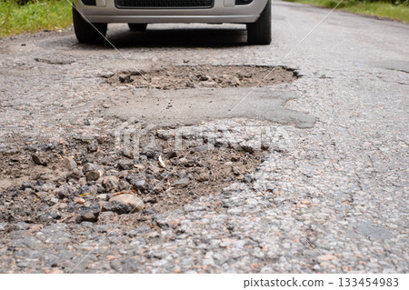 Car near many deep dangerous holes in asphalt surface. Concept of terrible condition of roads in poor countries Car near many deep dangerous holes in asphalt surface. Concept of terrible condition of roads in poor countries 133454983