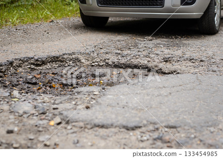 Car approaching big pothole in the countryside road. Dangerous situations while driving. Car in motion. 133454985