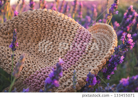 Straw hat resting in a field of lavender flowers. Close-up of a woven straw hat nestled among purple lavender blossoms Straw hat resting in a field of lavender flowers. Close-up of a woven straw hat nestled among purple lavender blossoms 133455071