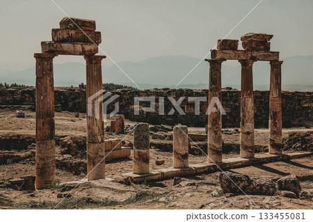 Ancient pillars in a historical site The image features three aged pillars, remnants of an ancient structure set against a rustic backdrop, hinting at a rich history. Ancient pillars in a historical site The image features three aged pillars, remnants of an ancient structure set against a rustic backdrop, hinting at a rich history. 133455081