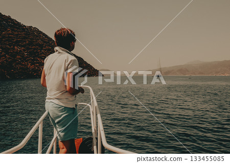 Woman on a boat enjoying a sunny day A person stands on a boat's railing, looking back at the camera with a smile, with a backdrop of sea, mountains. A person gazes out at the calm sea and islands. Woman on a boat enjoying a sunny day A person stands on a boat's railing, looking back at the camera with a smile, with a backdrop of sea, mountains. A person gazes out at the calm sea and islands. 133455085