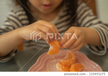 一個蹣跚學步的孩子把橘子皮上的白色筋膜剝掉，然後吃了起來。 133455275