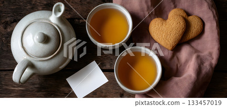 Teapot with two cups of tea and heart-shaped cookies on a rustic wooden table with copy space 133457019