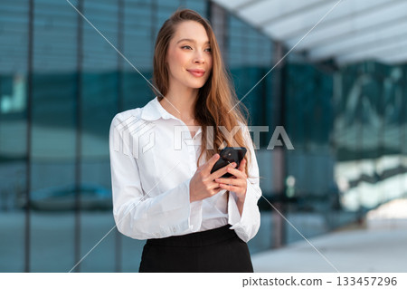 Smiling businesswoman using smartphone near glass 133457296