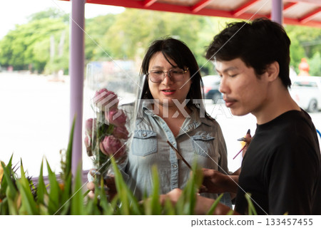 Two LGBTQ friends are at a Thai temple, offering incense and holding flowers while preparing to pray. They are experiencing a peaceful moment of spirituality and connection in a traditional setting. 133457455