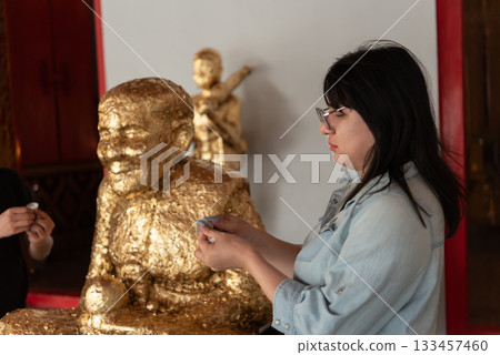 Two LGBTQ friends visiting a Thai temple for a spiritual practice. They are making merit by offering flowers and praying at the altar as part of their religious and cultural observance. 133457460
