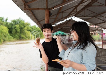 LGBTQ friends feeding fish at a Thai temple alms zone. The image shows an act of kindness and community engagement as the friends share a peaceful moment in a serene natural environment. 133457474