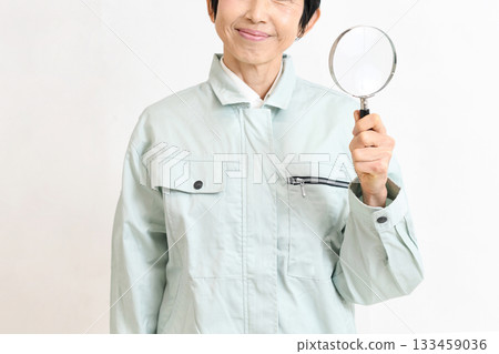 Middle-aged woman in work clothes looking at the camera with a magnifying glass Middle-aged woman in work clothes looking at the camera with a magnifying glass 133459036