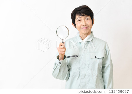 一位身穿工作服的中年婦女拿著放大鏡看著鏡頭。 133459037