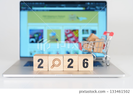 Happy New Year 2026 block with magnifying glasss and shopping trolley cart on table. E commerce, online shopping, finance, consumer economy and celebration concepts 133461502