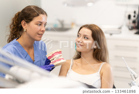 Female dentist tells a client about dental care and shows a model of the jaw Female dentist tells a client about dental care and shows a model of the jaw 133461898