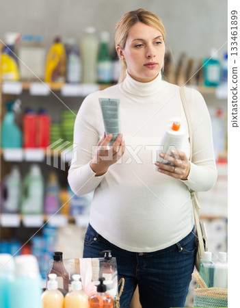 Thoughtful pregnant woman choosing sunscreen in personal care store 133461899