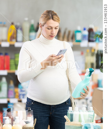 Pregnant woman scanning glass cleaner spray in household store 133461913