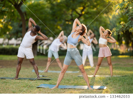 Multinational yoga enthusiasts with female coach perform Tiryaka Tadasana in park Multinational yoga enthusiasts with female coach perform Tiryaka Tadasana in park 133462033