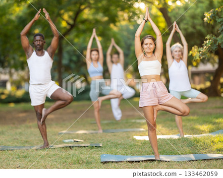 Girl performing one leg balancing pose during group yoga in park 133462059