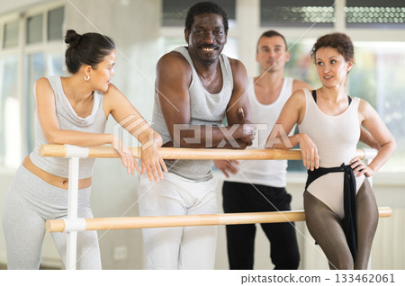 Smiling African American man relaxing with dancers at ballet barre Smiling African American man relaxing with dancers at ballet barre 133462061