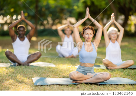 Woman meditating in lotus position at group yoga class in park 133462140