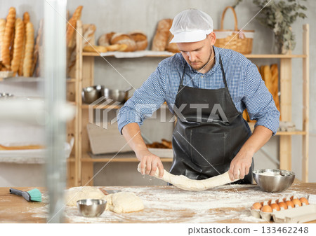 Guy works as baker in bakery, molds sausages from dough, rolls long round strips from dough Guy works as baker in bakery, molds sausages from dough, rolls long round strips from dough 133462248