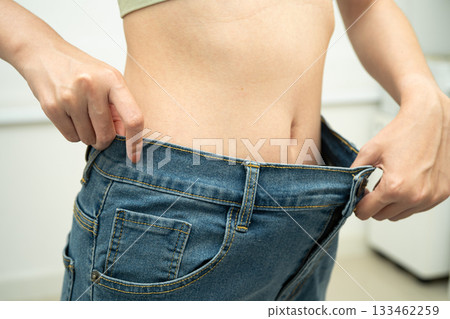 Young Asian woman losing weight wearing loose pants in oversize jeans. Young Asian woman losing weight wearing loose pants in oversize jeans. 133462259