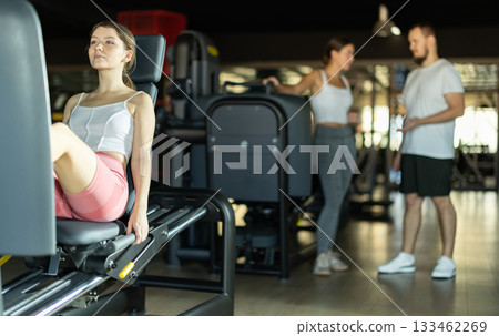 Slender athletic girl work out muscles of legs and thighs on simulator in fitness club 133462269