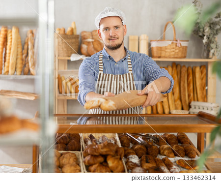 Man seller puts baguettes in paper bag for buyer, packs goods. Man seller puts baguettes in paper bag for buyer, packs goods. 133462314